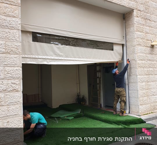 שני אנשים מתקינים סוכך בד חיצוני על מבנה